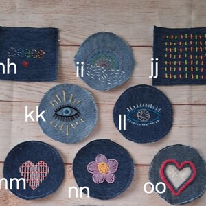 May include: A collection of denim patches with embroidered designs. The patches include a square patch with the word "peace", a circular patch with an eye design, and a heart-shaped patch. The patches are in shades of blue and feature colorful embroidery.