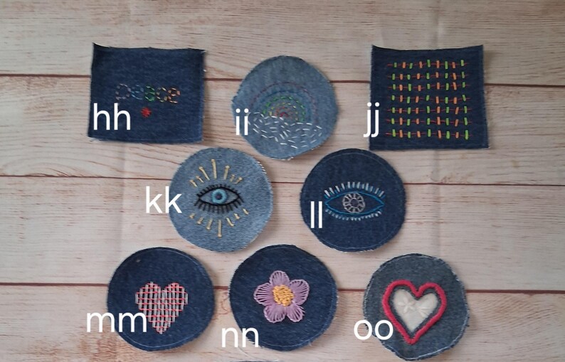 May include: A collection of denim patches with embroidered designs. The patches include a square patch with the word "peace", a circular patch with an eye design, and a heart-shaped patch. The patches are in shades of blue and feature colorful embroidery.