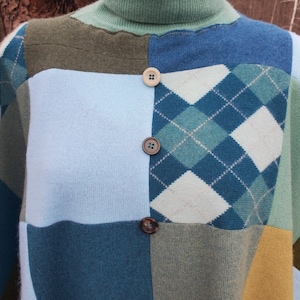 Könnte beinhalten: Ein Patchwork-Rollkragenpullover in Blau-, Grün- und Gelbtönen. Der Pullover hat eine Mischung aus einfarbigen und Argyle-Mustern mit drei braunen Knöpfen auf der Vorderseite. Der Kragen und der obere Teil sind einfarbig hellgrün.