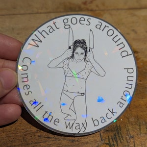 May include: A round sticker with a holographic finish. The sticker features a black and white illustration of a person holding two knives behind their head. The text "What goes around comes all the way back around" is written around the edge of the sticker.