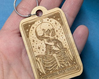 May include: A wooden keychain with a laser-engraved design of a skeleton with a thinking expression. The keychain features the text "PROFESSIONAL OVERTHINKER".