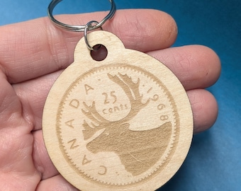 May include: A wooden keychain shaped like a Canadian 25-cent coin featuring a caribou with the text "CANADA 25 cents 1968".