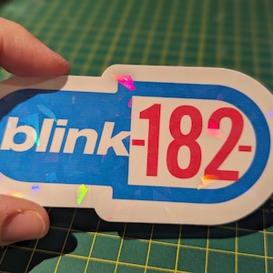 May include: A blue and white sticker with the text "blink-182" in red letters. The sticker has a holographic finish.