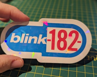 May include: A blue and white sticker with the text "blink-182" in red letters. The sticker has a holographic finish.
