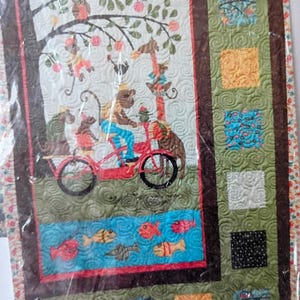 May include: A rectangular quilt featuring a central panel with a monkey riding a red bicycle, accompanied by other animals under a tree. The design includes a blue water section with fish, surrounded by a dark brown border and green patchwork squares.
