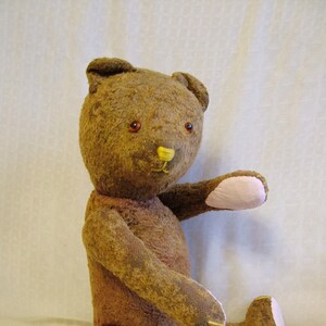 Puede incluir: Un oso de peluche marrón con detalles en fieltro rosa en sus patas y orejas. El oso tiene ojos de botón marrones y una nariz de fieltro amarilla.