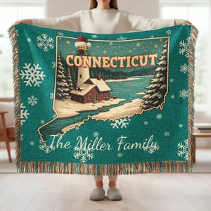 Può includere: Coperta turchese con una scena invernale di un faro nel Connecticut, con il contorno dello stato e fiocchi di neve. La coperta ha un bordo con frange e il testo "Connecticut" e "The Miller Family".