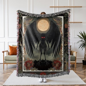 May include: A woven tapestry throw blanket features a dark, shadowy creature with glowing red eyes and outstretched wings. The creature is silhouetted against a full moon and a background of swirling clouds. The tapestry is framed by a decorative border with floral motifs.