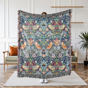 May include: A woven throw blanket with a blue background and a repeating pattern of stylized flowers, birds, and leaves. The pattern is in shades of green, yellow, red, and pink.
