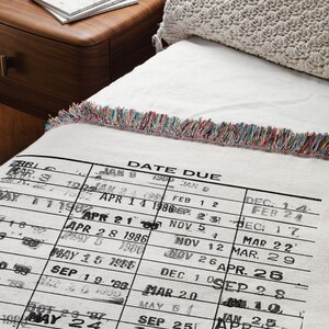 May include: A white woven throw blanket with a black and white printed calendar design. The calendar shows dates and months from January 1986 to May 1987. The blanket has a colorful fringe border.