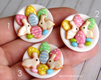 May include: Three miniature white plates with pastel colored bunny shaped cookies, decorated Easter eggs and candy. The plates are numbered 1, 2, and 3.