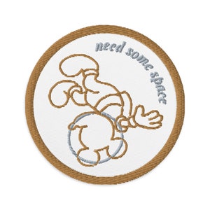 May include: A brown and white embroidered patch featuring a cartoon character holding a hoop with the text "need some space".