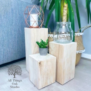 May include: Three whitewashed wooden cube risers, the largest with a clear glass vase, the middle with a small potted succulent, and the smallest with a geometric copper candle holder.