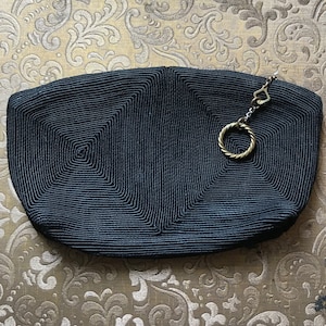 May include: A black woven clutch bag with a gold chain and ring detail.