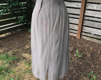 May include: A brown high-waisted skirt with a straight silhouette and a center back slit. The skirt is made of a textured fabric and has a high waistline.
