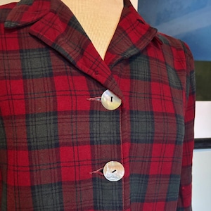 May include: A red and green plaid shirt with a button-up front and long sleeves. The shirt has five buttons down the front.