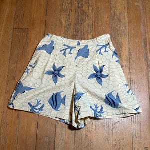 May include: A pair of cream-coloured shorts with a blue and white sea life print. The print features fish, starfish, and coral.