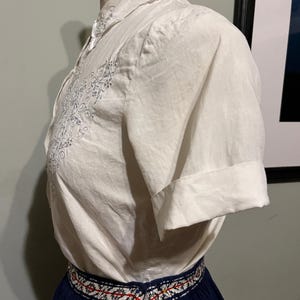 May include: A white embroidered short-sleeved blouse with a navy blue skirt with a white and red embroidered waistband.