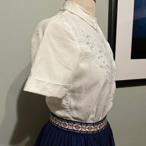 May include: A white short-sleeved blouse with embroidered floral details and a navy blue skirt with a white and red embroidered waistband.