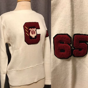 May include: White sweater with a red felt letter 'C' with a gold lyre on the front and a red felt '65' on the sleeve.