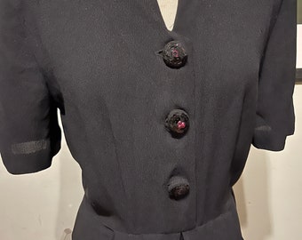 May include: A black dress with a v-neckline and three black buttons with pink centers. The dress has short sleeves and a fitted bodice.