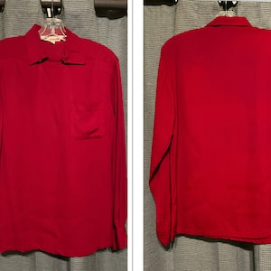 May include: A long-sleeved, solid red button-down shirt with a single pocket on the left side. The shirt is hanging on a hanger.