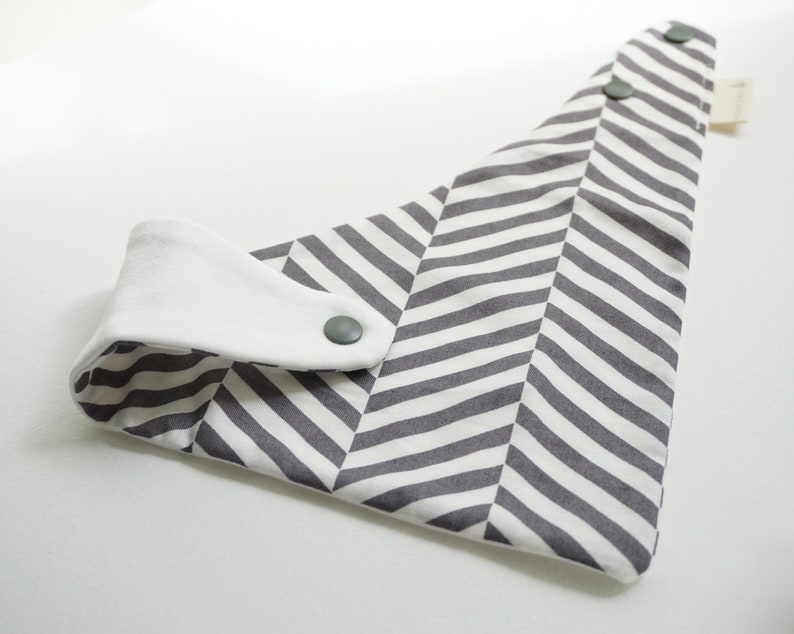 May include: A gray and white chevron patterned bib with a white cotton snap closure and two gray snaps.