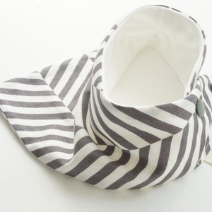 May include: A gray and white striped fabric baby bib with a white lining and two gray buttons. The bib has a label that says "MONTERY".