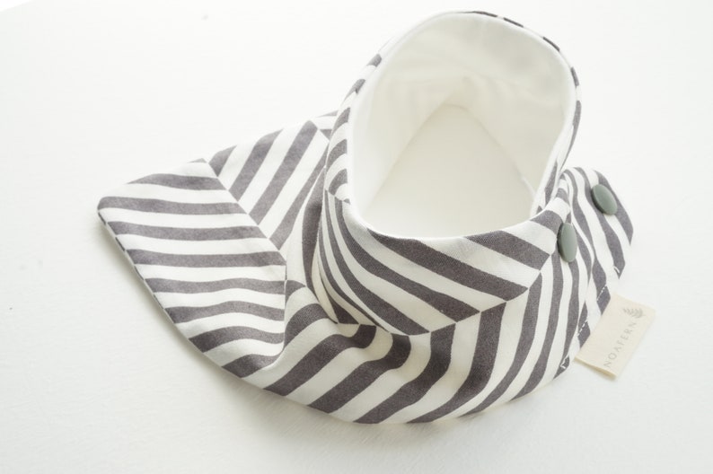 May include: A gray and white striped fabric baby bib with a white lining and two gray buttons. The bib has a label that says "MONTERY".
