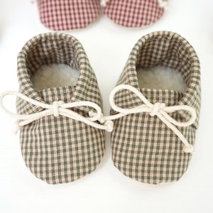 May include: A pair of green and beige gingham baby shoes with white laces tied in a bow.