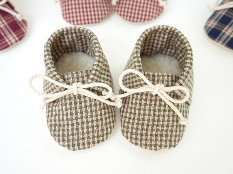 May include: A pair of green and beige gingham baby shoes with white laces tied in a bow.