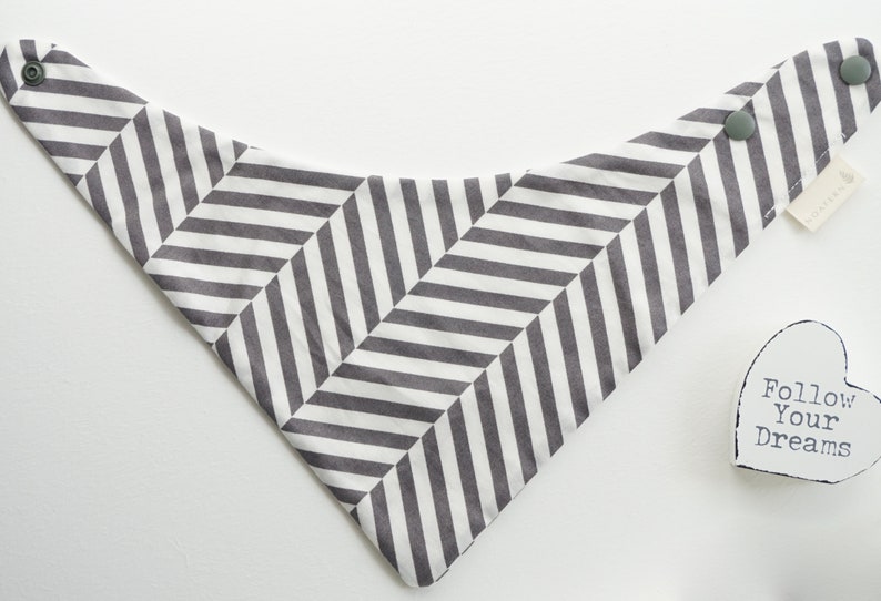 May include: A white and gray chevron patterned bandana with two snap closures. The bandana has the text "Follow Your Dreams" on a white heart-shaped tag.