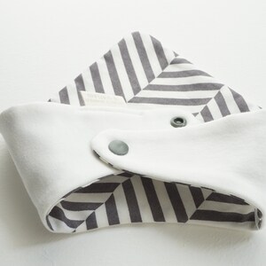 May include: A white and gray striped baby bib with two snap closures. The bib is reversible with a white side and a gray and white striped side.