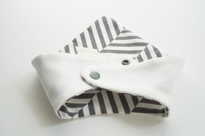 May include: A white and gray striped baby bib with two snap closures. The bib is reversible with a white side and a gray and white striped side.