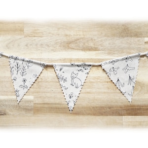 May include: A white fabric banner with black illustrations of flowers, leaves, and a small animal. The banner is strung on a wooden surface.