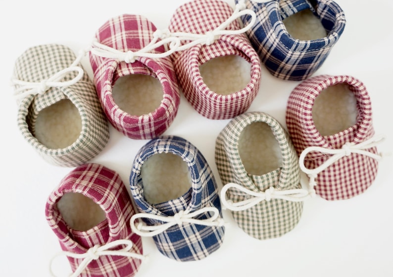 May include: Eight pairs of baby booties in various plaid patterns, including red and white, blue and white, and green and white. The booties have white laces and are made of soft fabric.