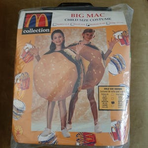 Könnte beinhalten: Ein McDonald's Big Mac Kostüm für Kinder. Das Kostüm ist ein brauner und gelber Overall mit einem Sesambrötchen-Oberteil und Salat- und Tomaten-Details. Das Kostüm ist in den Größen Kleinkind (2-4), klein (4-6), mittel (8-10) und groß (12-14) erhältlich.