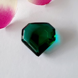 May include: A dark green faceted gemstone with a diamond shape.