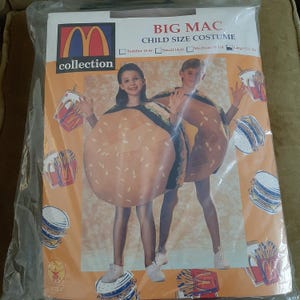 Könnte beinhalten: Ein Big Mac Kostüm für Kinder. Das Kostüm ist ein brauner und gelber Burger mit Sesamkörnern. Das Kostüm ist in den Größen Kleinkind (2-4), klein (4-6), mittel (6-10) und groß (12-14) erhältlich.
