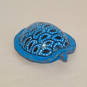 May include: A blue turtle figurine with black and white painted designs on its shell. The turtle has a red painted head and feet.