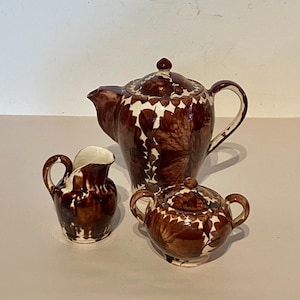 May include: A brown and white ceramic tea set with a teapot, creamer, and sugar bowl. The set features a floral pattern.