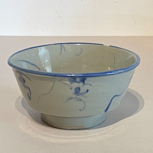 May include: A small, white ceramic bowl with a blue rim and blue floral designs. The bowl has a slightly chipped rim.