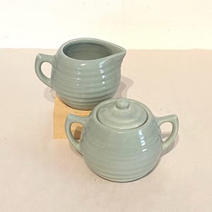 May include: A set of two ceramic creamer and sugar containers in a light green color with a ribbed design.
