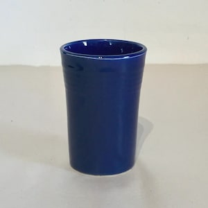 Może przedstawiać: Głęboki niebieski kubek ceramiczny o gładkim, zaokrąglonym kształcie. Kubek idealnie nadaje się do przechowywania drobnych przedmiotów lub do celów dekoracyjnych.