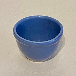 May include: A small, light blue ceramic bowl. The bowl is round and has a smooth, glazed finish.