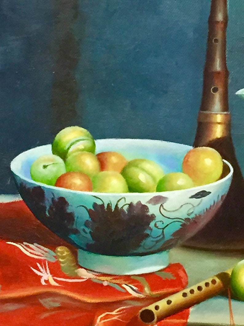 May include: A blue and white porcelain bowl filled with green and yellow fruit. The bowl is sitting on a red cloth with a wooden flute and a brown musical instrument.