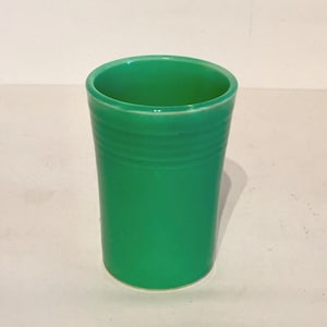Puede incluir: Un vaso de beber de cerámica verde con un borde liso y redondeado y una base ligeramente acampanada. El vaso tiene un patrón texturizado sutil alrededor del medio.