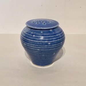 May include: A blue ceramic jar with a lid and white speckles. The jar has a round body and a slightly flared top. The lid has small holes for ventilation.