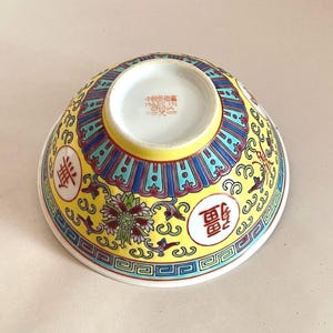 May include: A yellow ceramic bowl with a blue and red floral design and Chinese characters. The bowl is marked "Made in China" on the bottom.