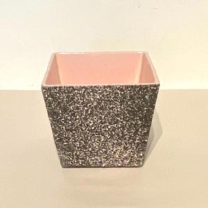 May include: A square ceramic planter with a speckled black and white exterior and a solid pink interior.